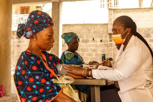 A healthcare worker checks blood pressure of an elderly woman in a rural clinic setting.